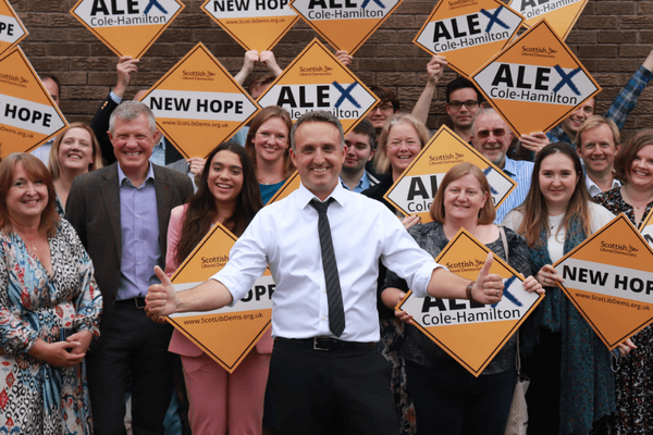 Photo of Alex Cole-Hamilton in front of a group of Lib Dem members holding up orange diamonds