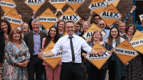 Photo of Alex Cole-Hamilton in front of a group of Lib Dem members holding up orange diamonds