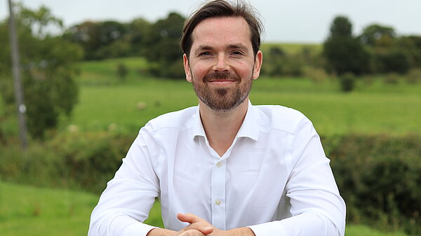 Adam Harley smiling while leaning on a fence with green fields in the background